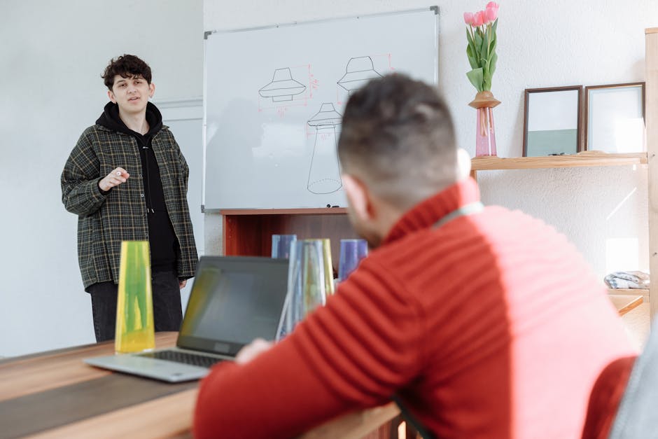 Two men in a casual office setting presenting on a whiteboard with visible drawings.